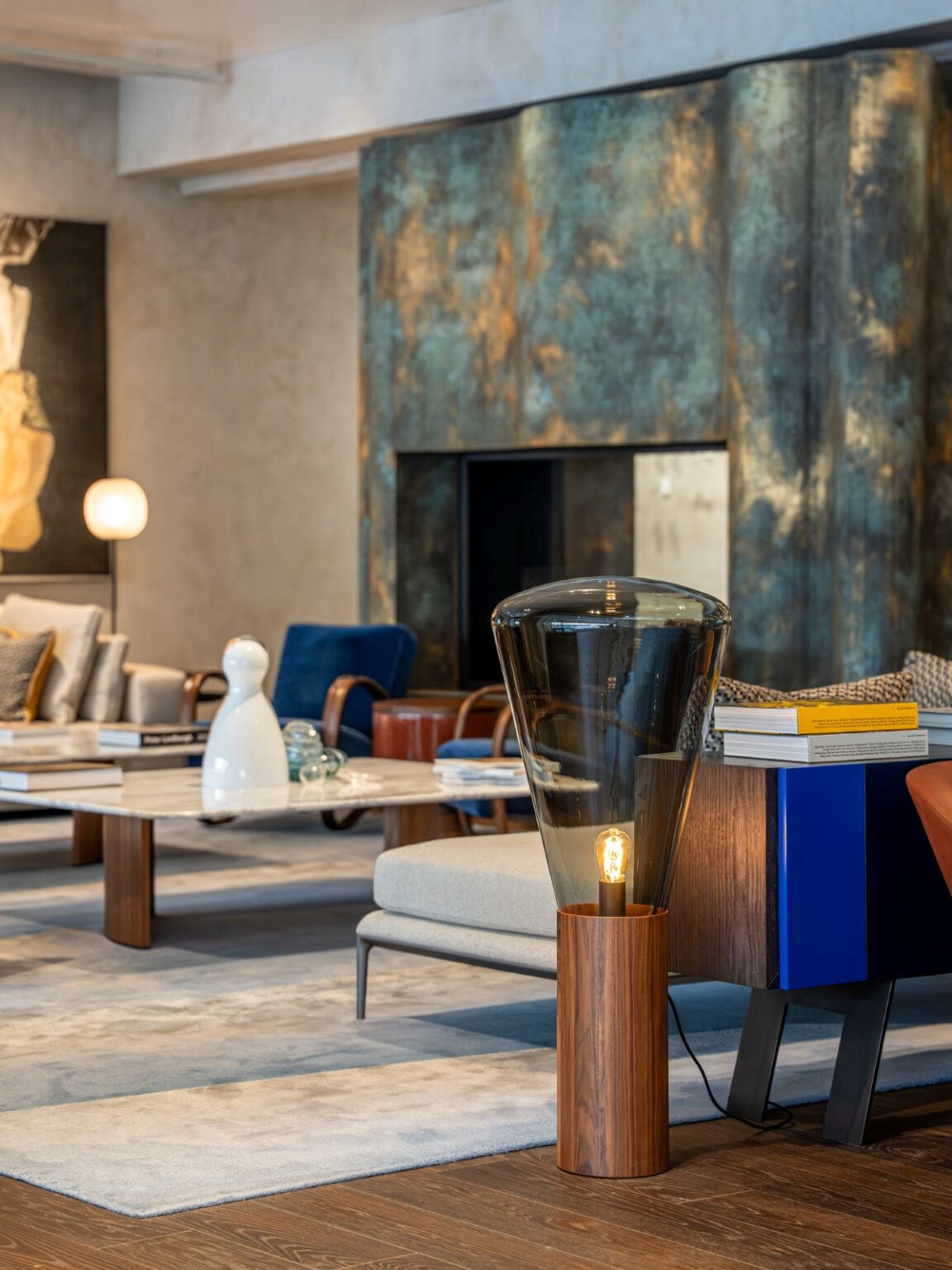 Elegant living room in blue and neutrals, Brokis Muffins floor lamp, artful coffee table, and textured metal fireplace.