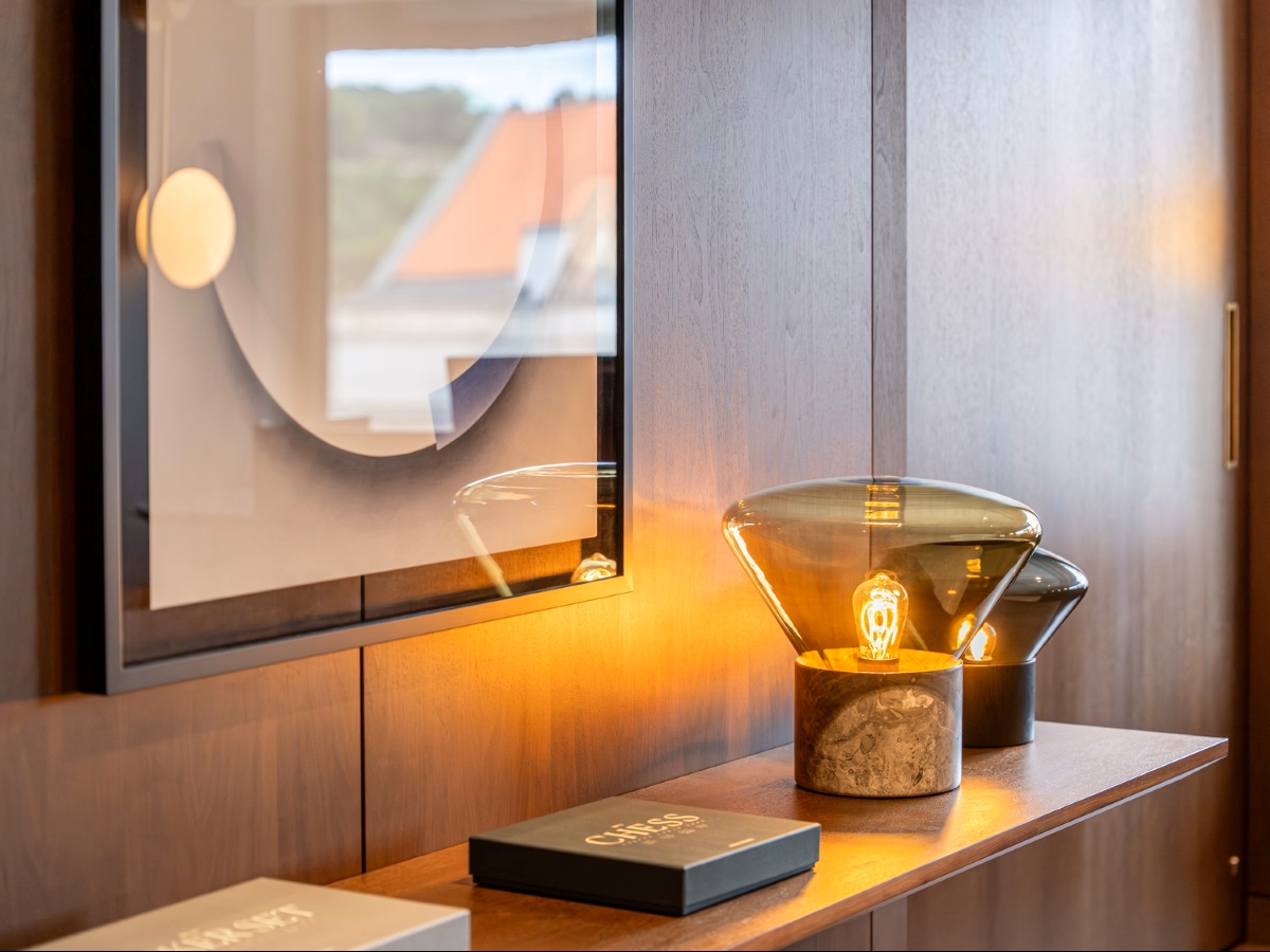 A modern sideboard displays Brokis Muffins table lamp, marble base, decor accents, and abstract art above.