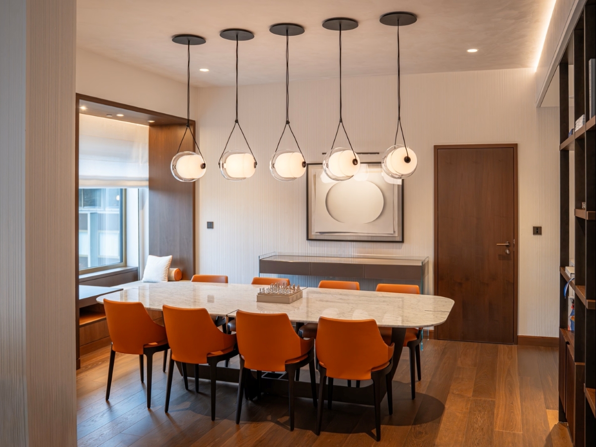 A modern dining room with a marble table, eight orange chairs, and Brokis Capsula Single pendants above.