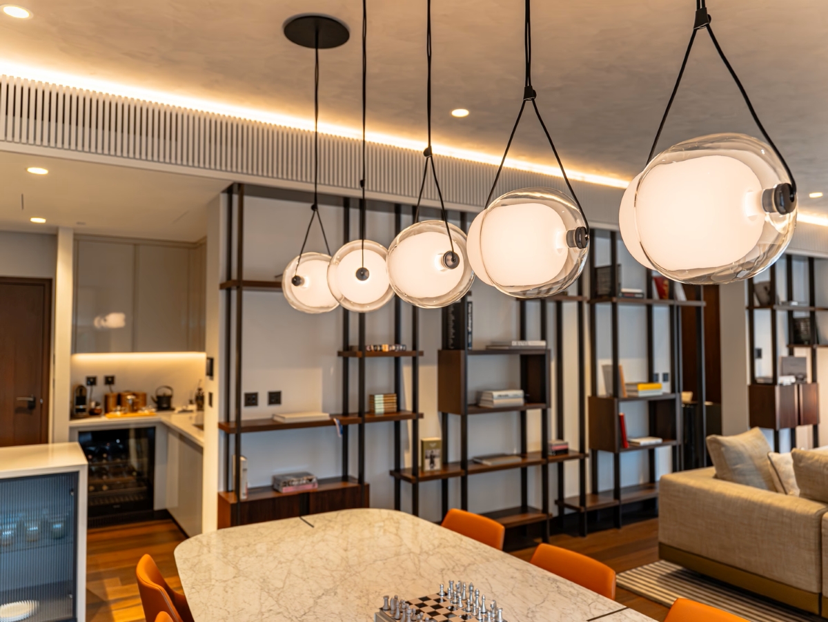 A marble table, vibrant orange chairs, and Brokis Capsula Single pendants elevate this luxurious dining space.