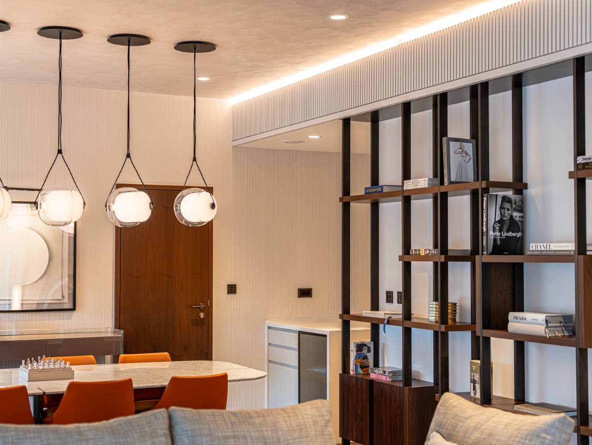 A modern living-dining space with Brokis Capsula Single pendants, orange dining chairs, and warm, luxurious accents.