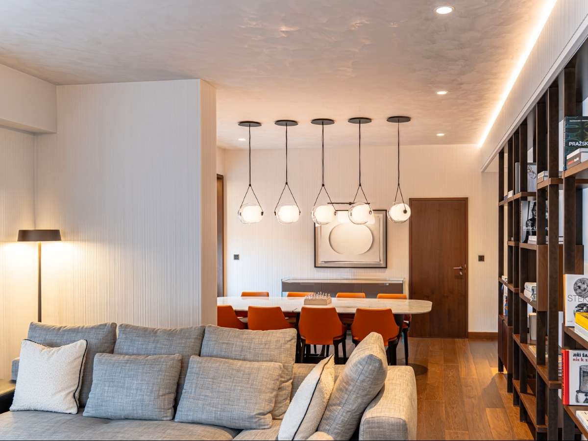 Living-dining area with a grey sectional, Brokis Capsula Single pendants, orange chairs, art and curated library wall.