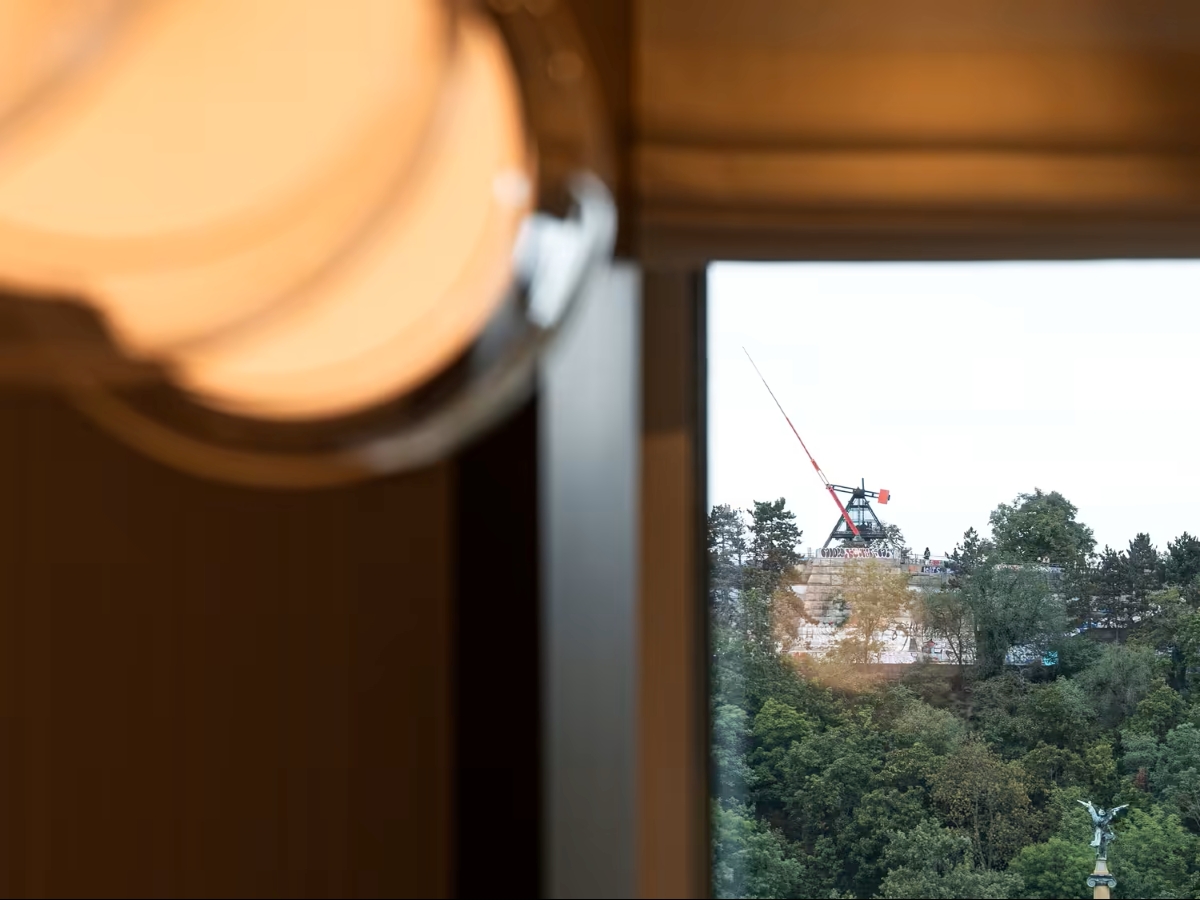 A blurred, Brokis Capsula Single pendant glows at left; beyond the window, lush hills and a distant statue shimmer.