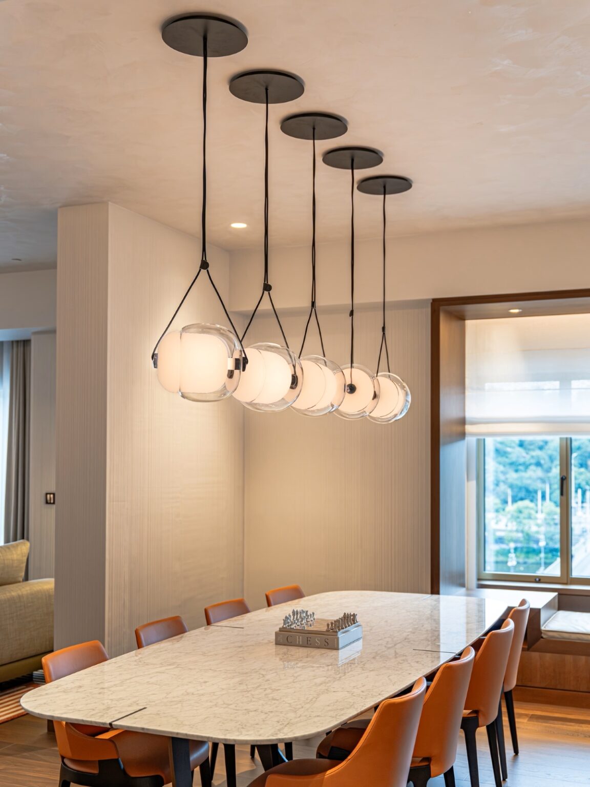 A modern dining room with a white marble table, tan leather chairs, Brokis Capsula Single pendants, and airy decor.