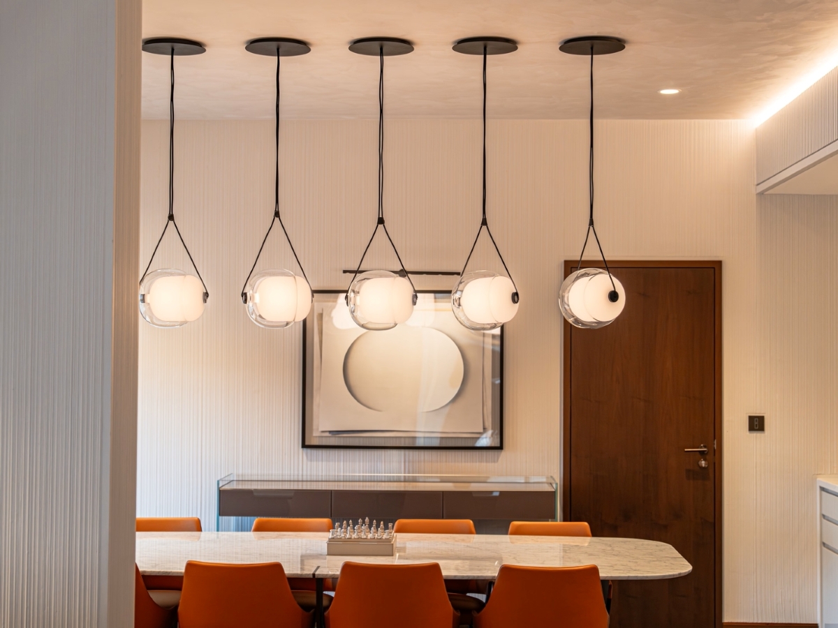 Luxury dining room with a marble table, burnt-orange chairs, and Brokis Capsula Single pendants above the setting.