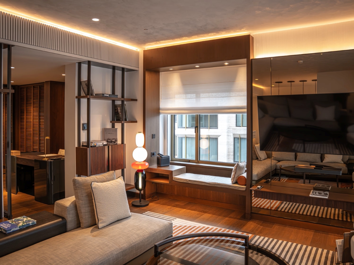 Sleek living room with wooden floors, neutral sofas, window seat, glass coffee table, designer lamp, and city views.