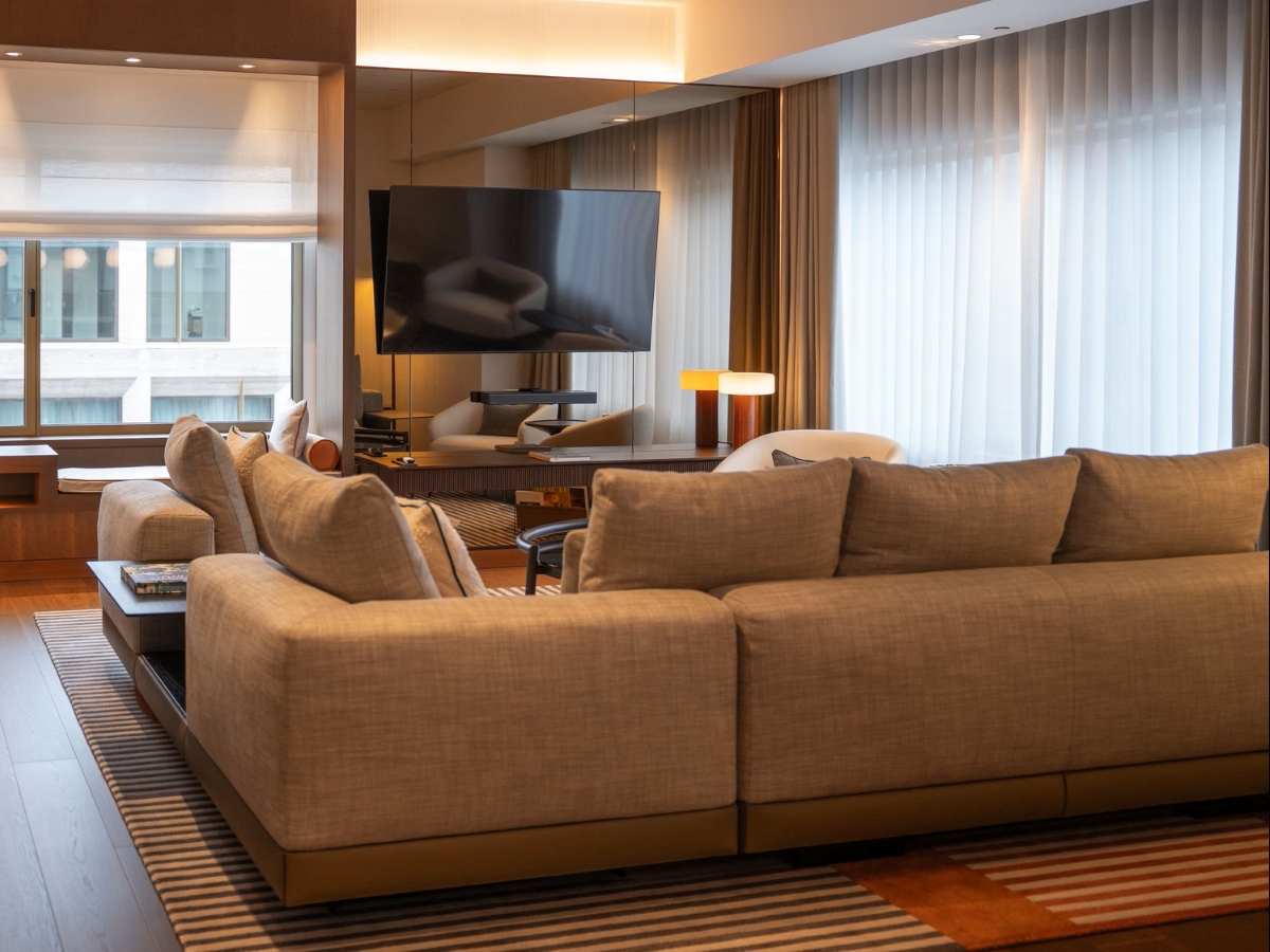 A luxe living room with beige sofas, striped rug, sheer curtains, table lamp, and sun-washed windows.
