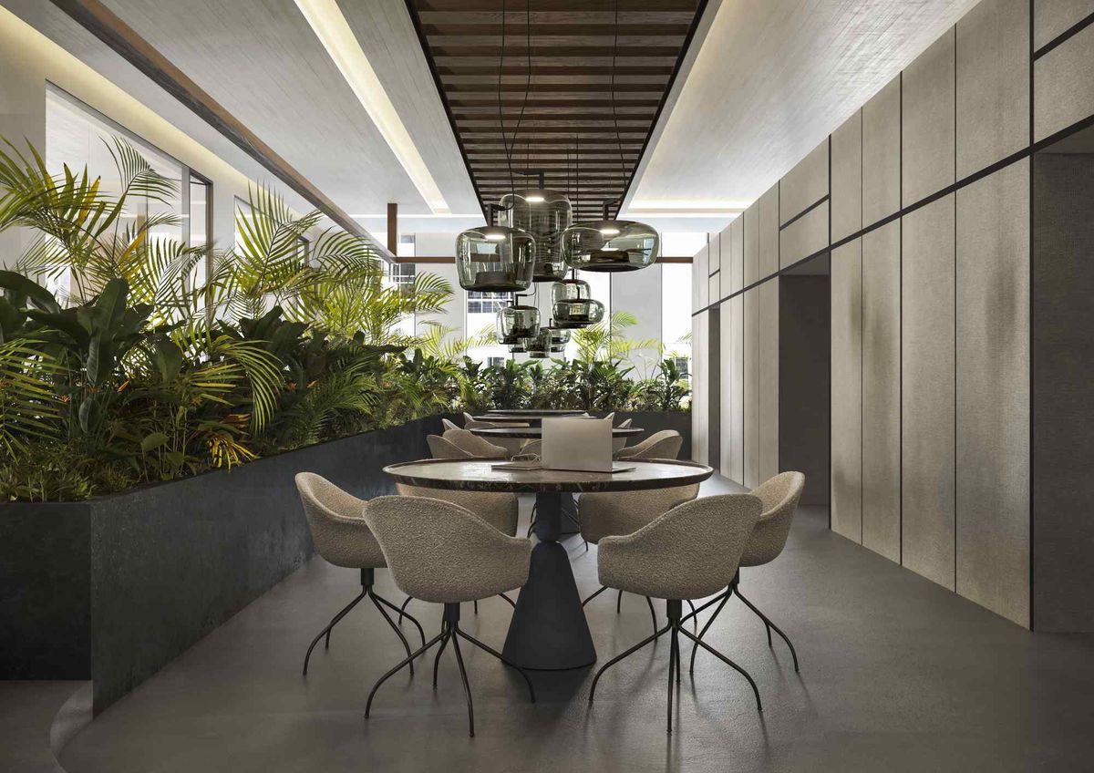 Elegant dining area with round tables, cushioned chairs, Brokis Double pendant lights, and lush green plant dividers.