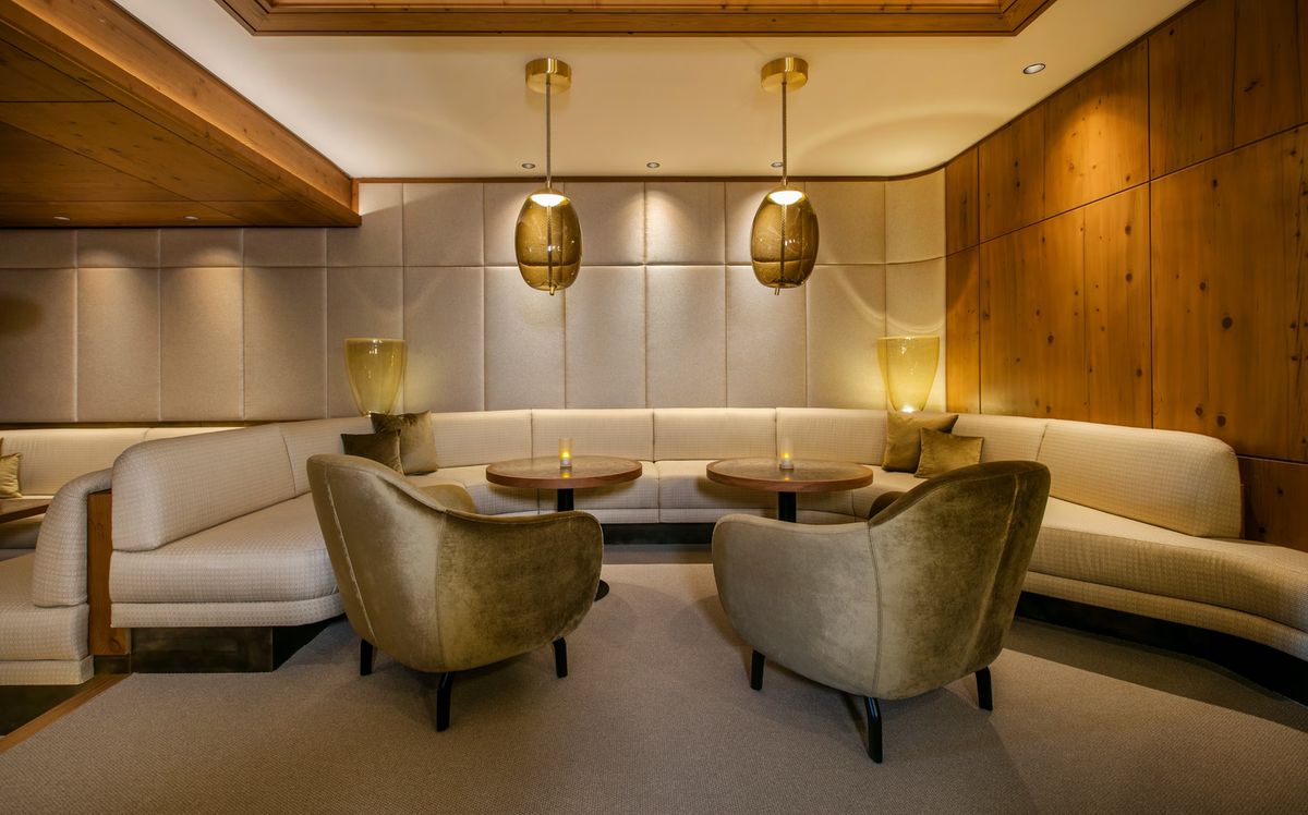 A luxurious lounge with beige curved sofas, velvet armchairs, Brokis Knot Uovo pendants, and warm ambient lighting.