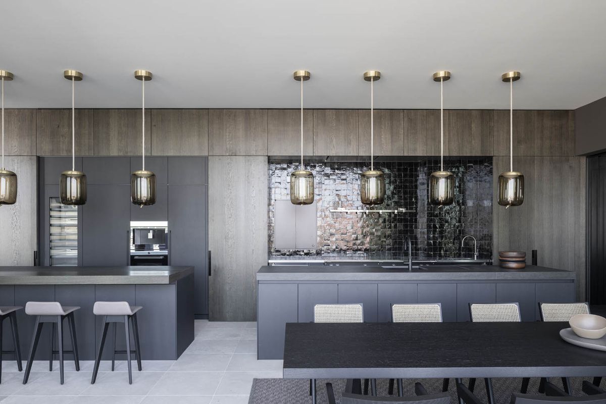Modern kitchen with grey cupboards, black-tiled splashback, and Brokis Knot pendants over the island. Elegant luxury style.