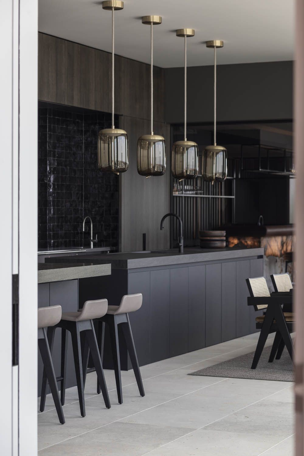 A kitchen with dark cupboards, splashback, and worktops. Four Brokis Knot Cilindro pendants grace the breakfast bar.