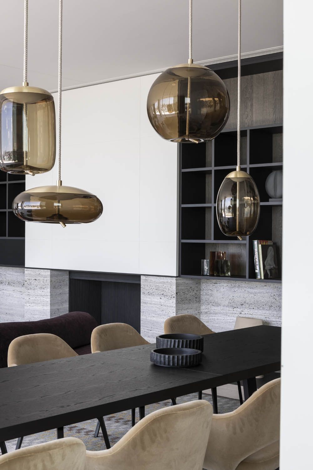 A modern dining room with a black table, beige chairs, and Brokis Knot pendants. Shelves display artful décor.