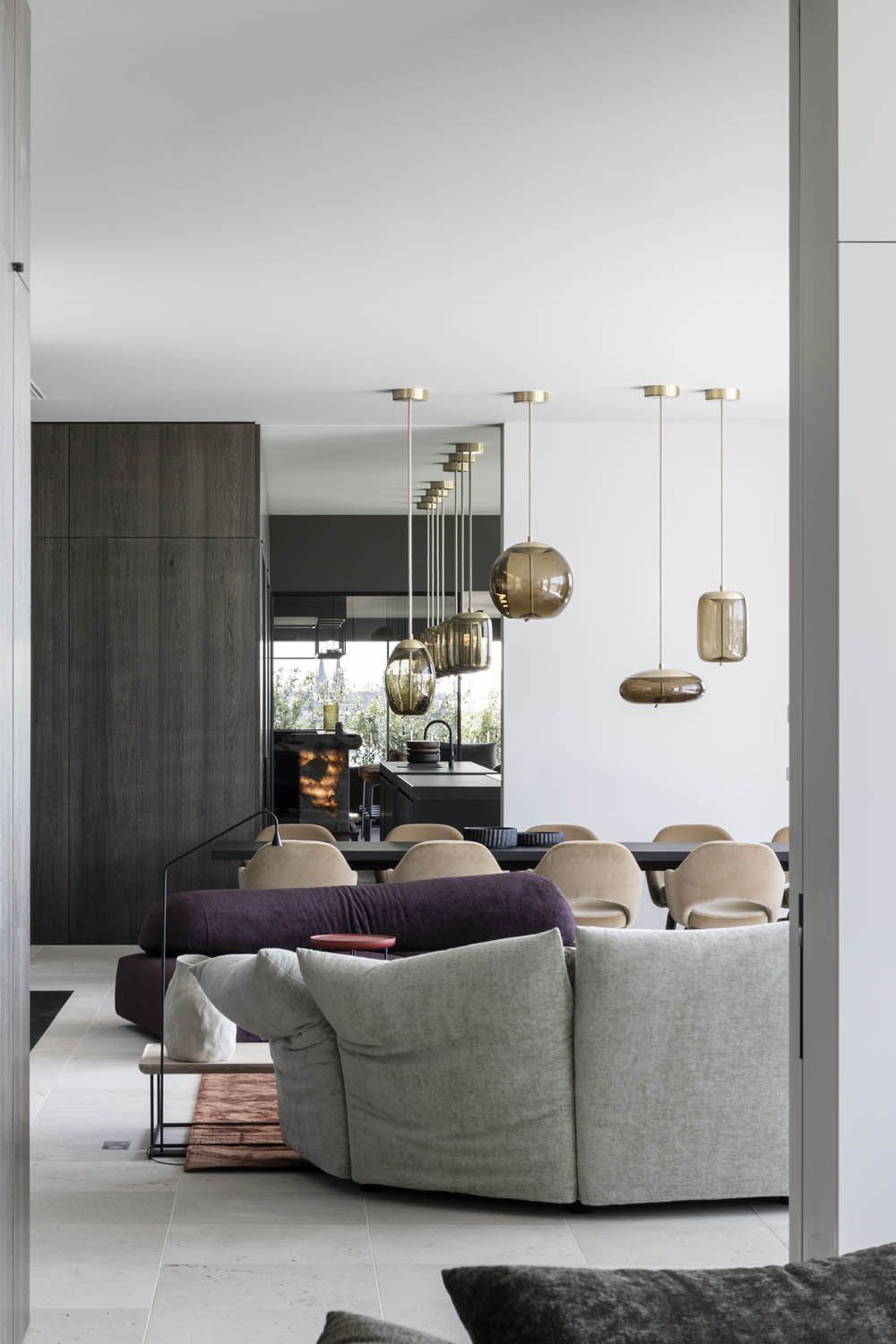 Luxurious open-plan space with plush grey and purple sofas, beige dining set, Brokis Knot pendants, and rich dark wood.