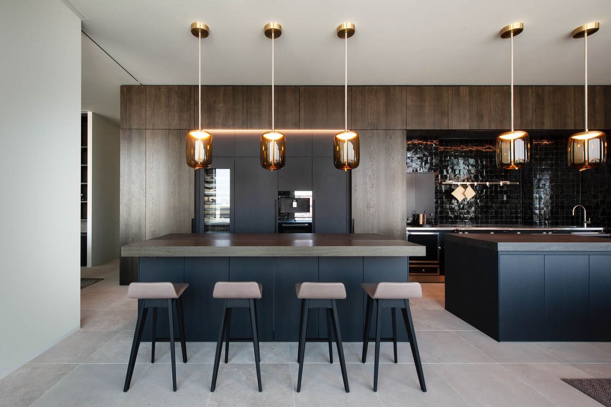 Modern kitchen with a large island, four plush bar stools, Brokis Knot Cilindro pendants, dark wood and black tile.