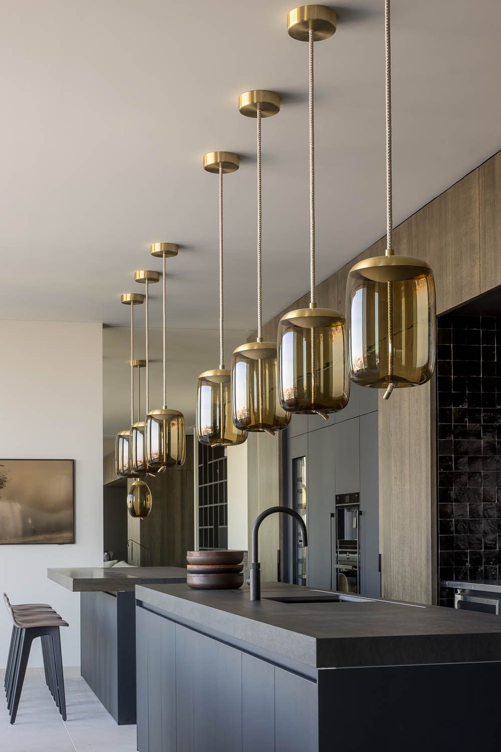 Modern kitchen with dark worktops, wooden cabinetry, and Brokis Knot Cilindro pendants over a peninsula; sleek and elegant.