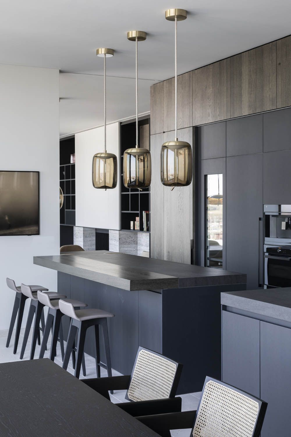 Sleek kitchen with matt black cabinetry, Brokis Knot Cilindro pendants, luxe island seating, and woven dining chairs.