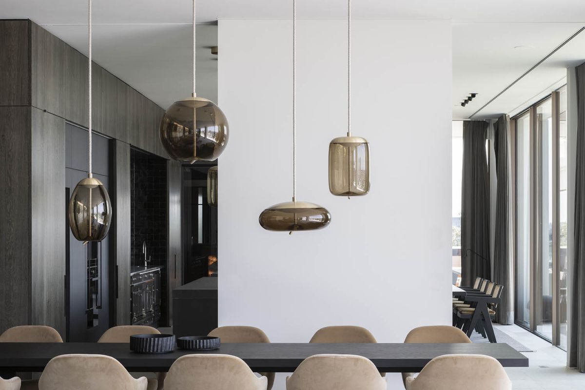 A dining area features beige chairs, a dark table, Brokis Knot pendants, and sleek cabinetry.