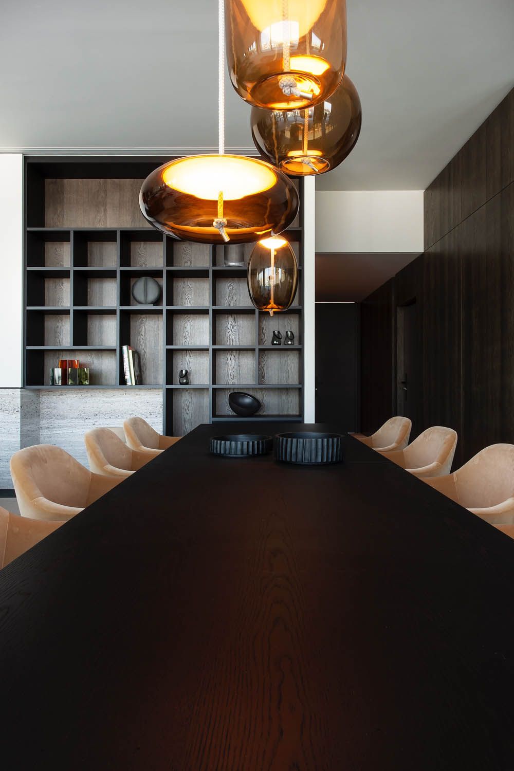 A modern dining room with a long black table, beige chairs, and Brokis Knot pendants overhead.