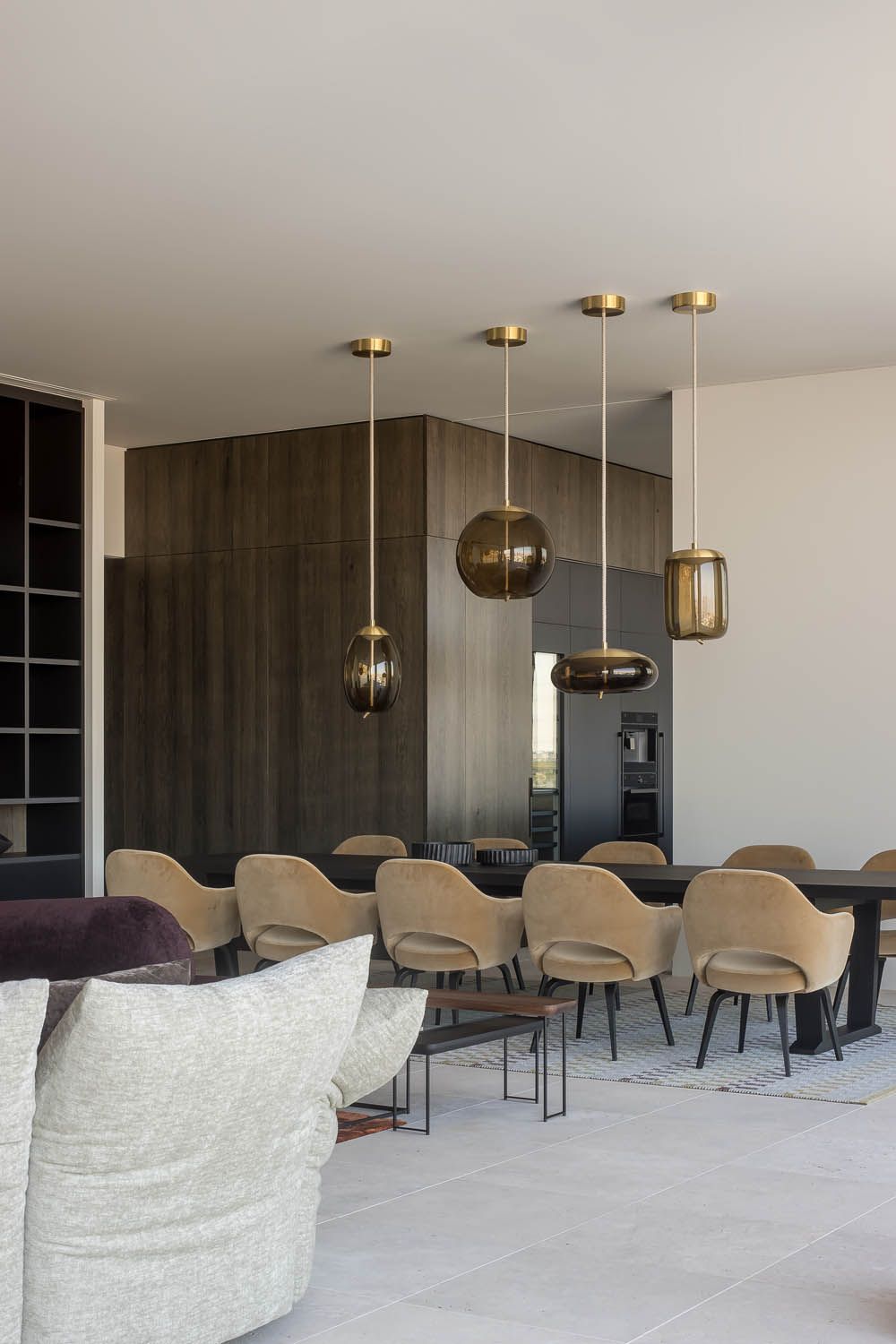 A modern dining area with a black table, ten beige velvet chairs, and four Brokis Knot pendants.
