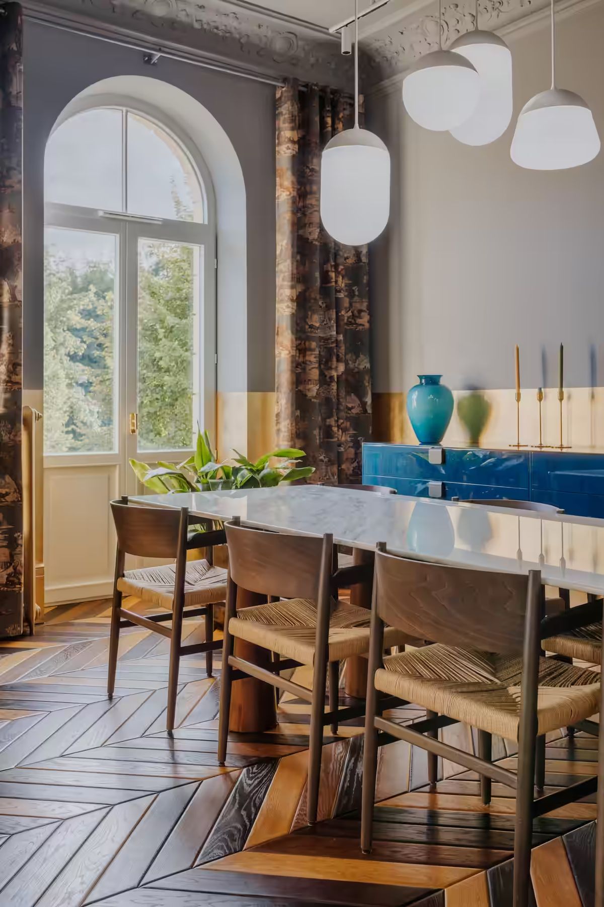 Elegant dining room with herringbone floor, long table, blue sideboard, gold candlesticks, and Brokis Planets 6 Set.