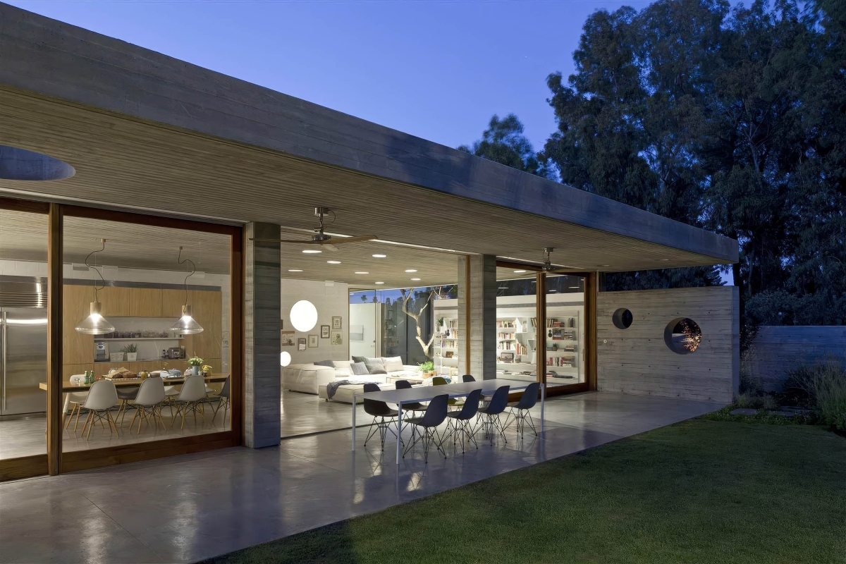 A modern home reveals a chic interior. Brokis Muffins pendants above a long dining table overlooks lush grounds at twilight.