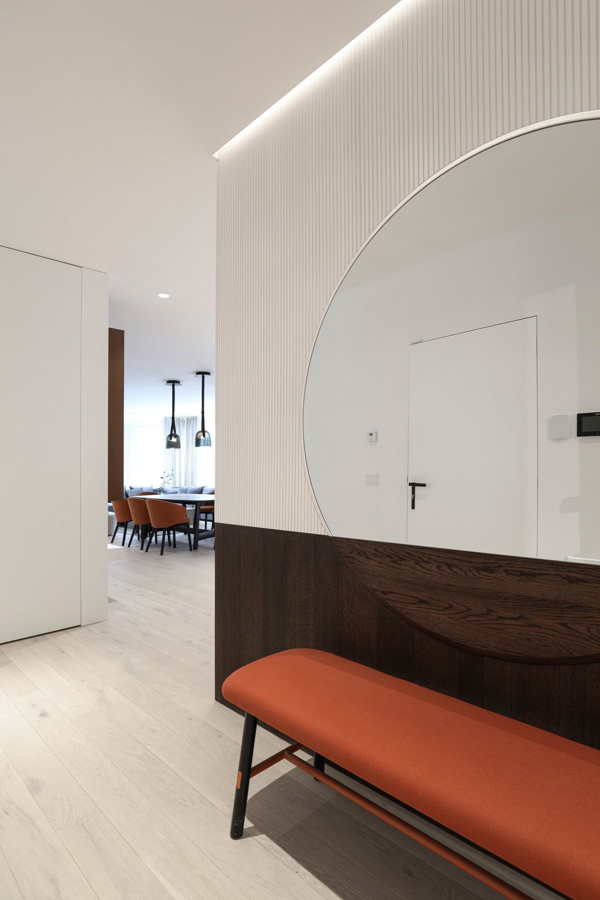 A chic entrance with light wooden flooring, and a round mirror above a bench. Brokis Mona Medium pendants visible beyond.
