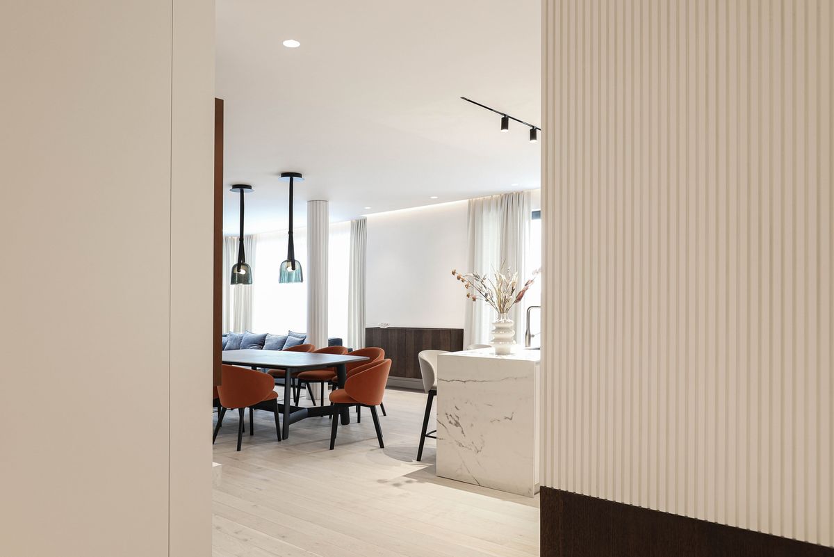 Elegant open-plan living and dining area with marble island, Brokis Mona Medium Pendants, and sheer-draped windows.