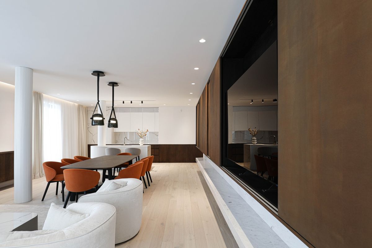 A luxurious, open-plan space with dark wood dining, orange chairs, Brokis Mona Medium Pendants, and expansive windows.