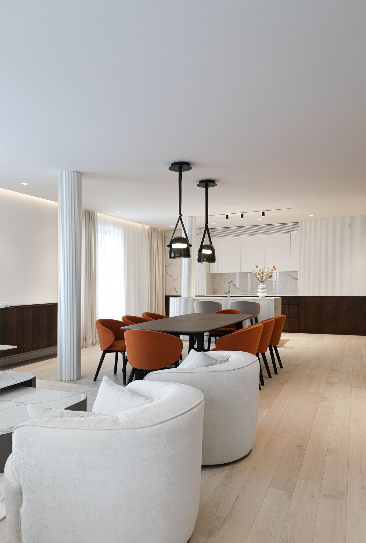 Modern open-plan space with dark oval dining table, orange chairs, Brokis Mona Medium Pendants, and sleek kitchen.