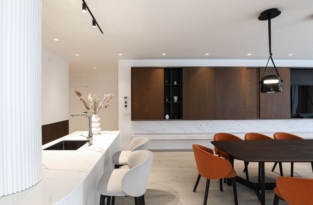 A dining kitchen with white marble, pale wood, Brokis Mona Pendants above a dark table, luxe chairs, and elegant accents.