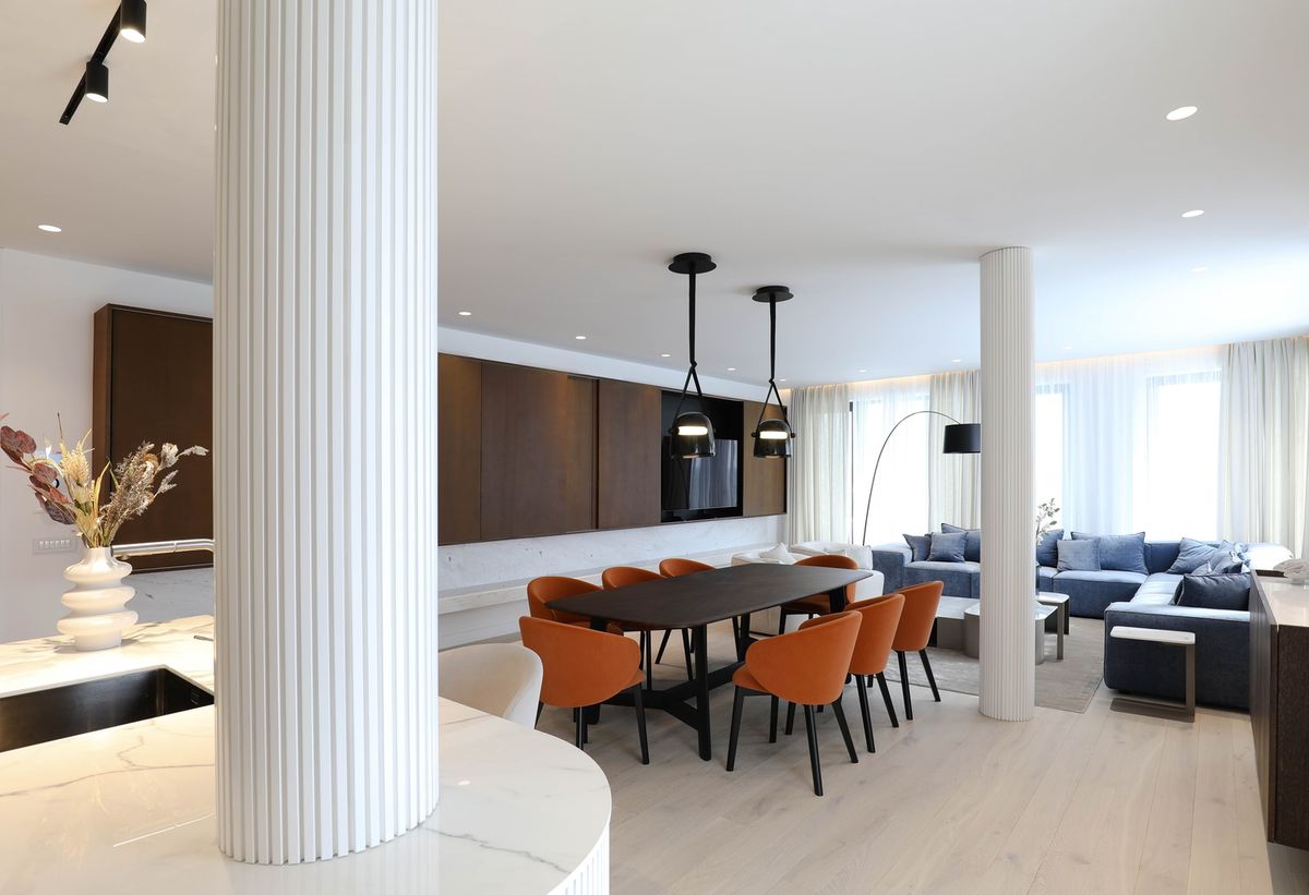 Elegant open living space with dark wood dining, orange chairs, black Mona Medium Pendants, marble, and sheer-draped windows.
