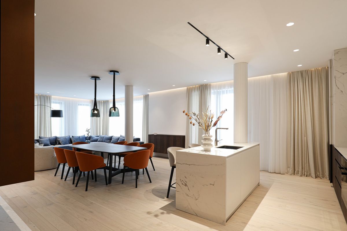 Luxurious open-plan space with marble island, Brokis Mona Medium Pendants, chic orange chairs, and sheer-lit seating area.
