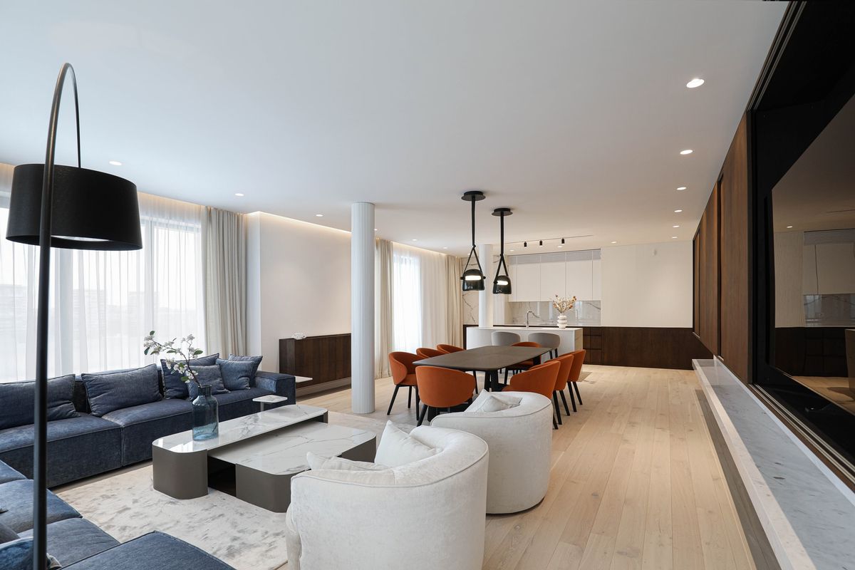 Open-plan living and dining area with light wood floors, navy sofa, Brokis Mona Medium pendants, and minimalist kitchen.