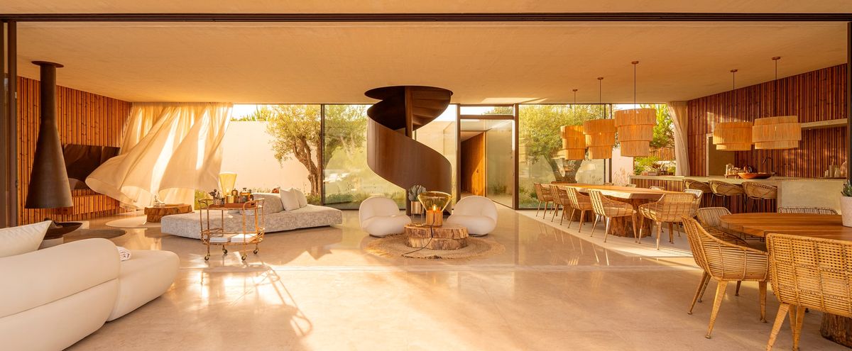 A sunlit, living-dining area with earthy tones, Brokis Muffins lighting, a floating fireplace, and sculptural staircase.
