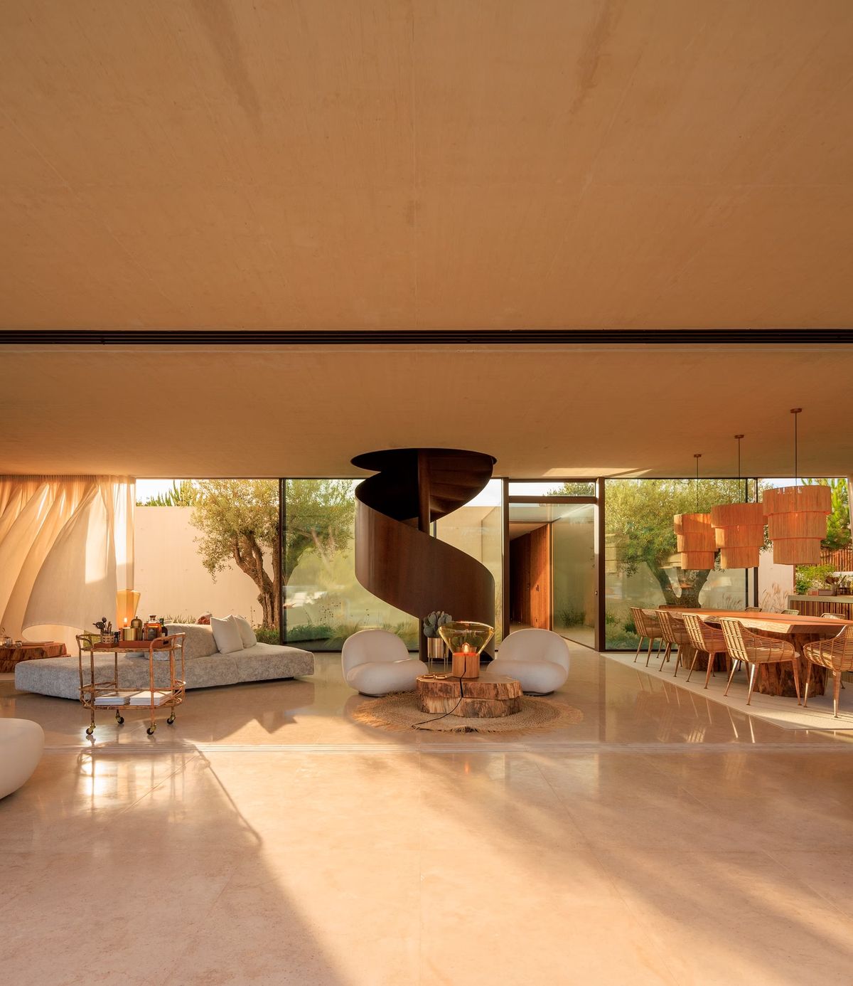 Sleek, sunlit living-dining space with sculptural wooden spiral stairs, glass walls, neutral decor, and Brokis Muffins lamps.