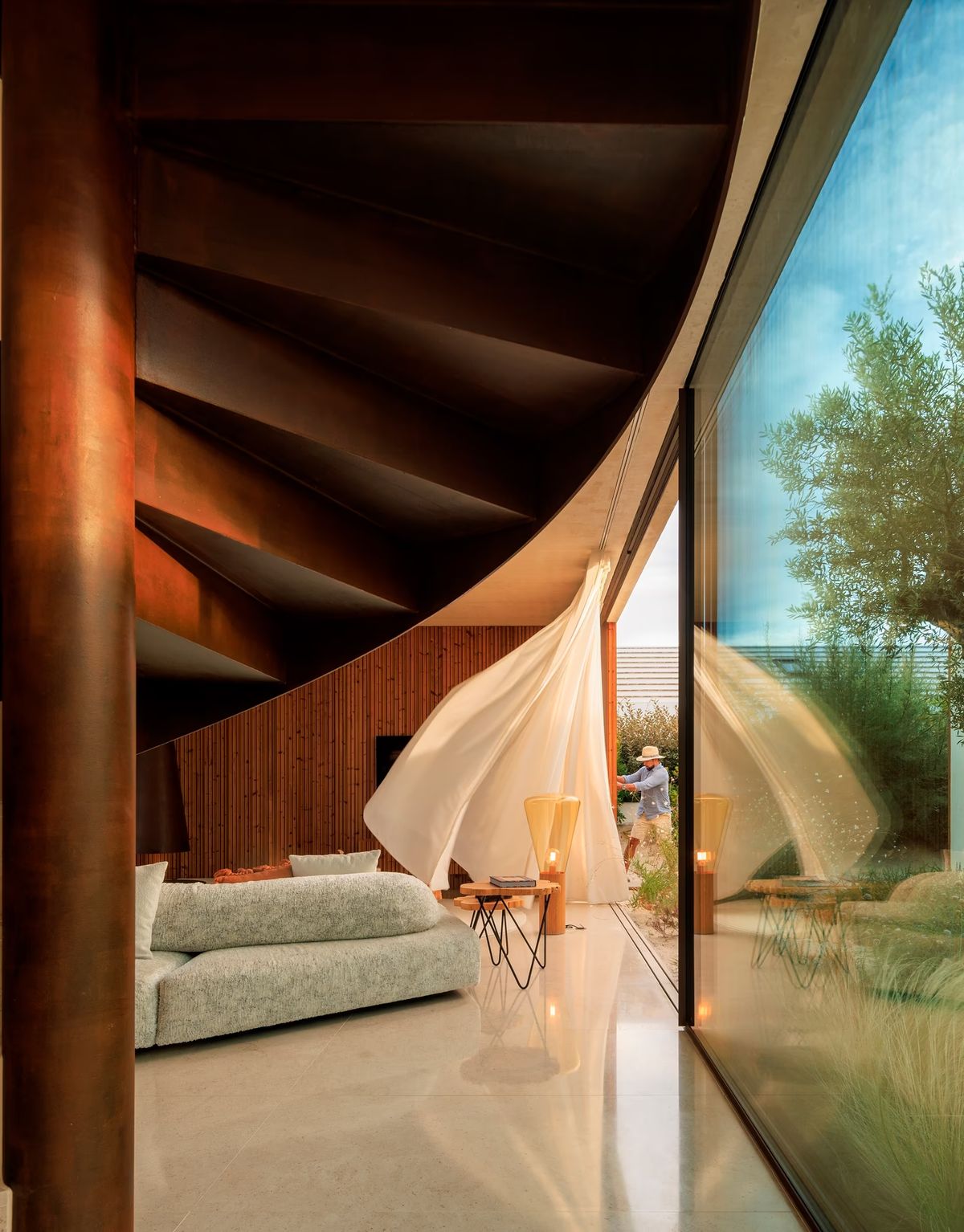 A modern living room with a spiral staircase, billowing white curtains, Brokis Muffins floor lamps, and garden views.