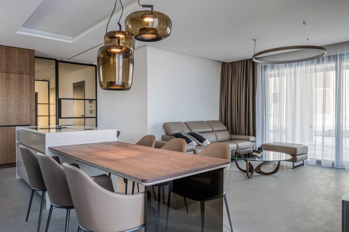 An open-plan lounge boasts brown Brokis Double pendants, taupe dining chairs, a beige corner sofa, and neutral décor.