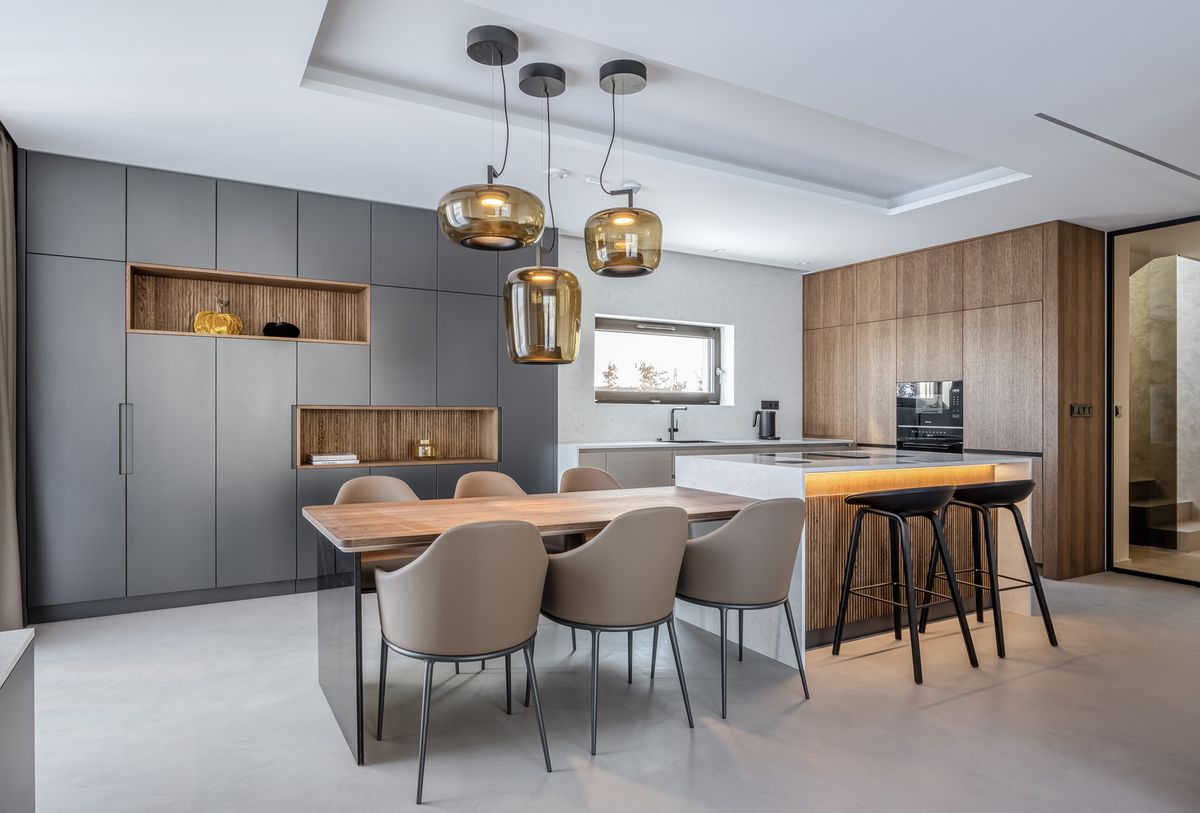 Luxury kitchen with grey and wood cupboards, marble island, Brokis Double pendants, and elegant beige dining chairs.
