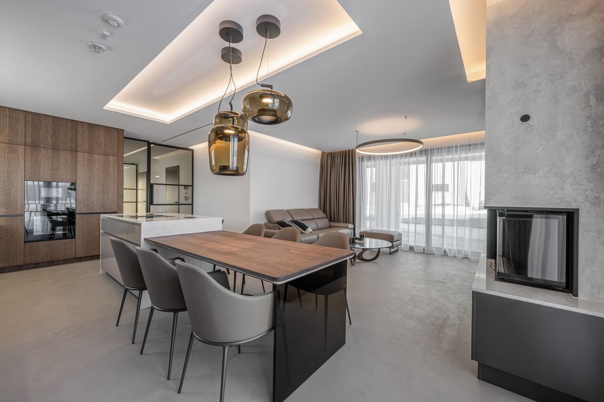 A modern luxury space with a marble island, Brokis Double pendants, beige corner sofa, and airy floor-to-ceiling windows.