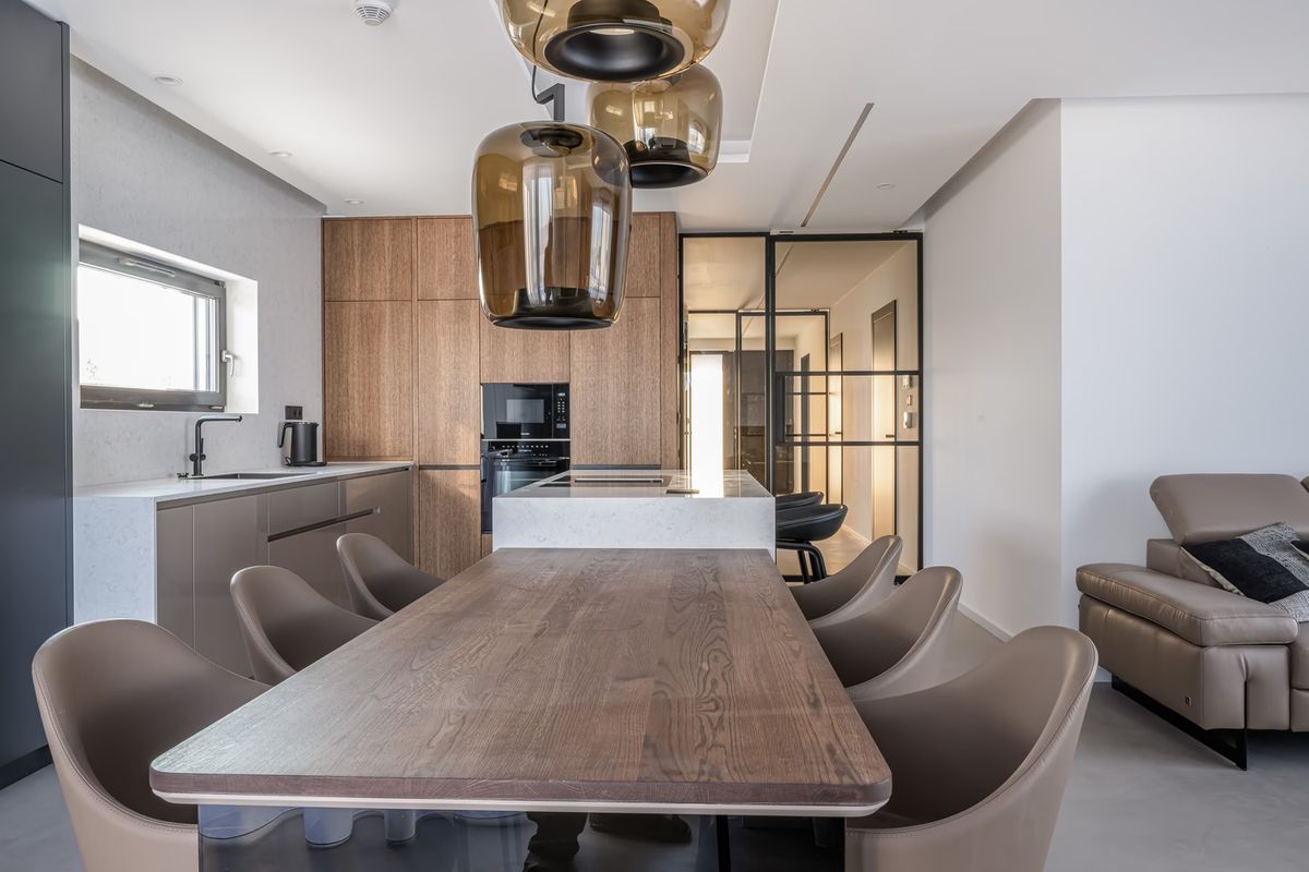 Sleek kitchen and dining space with a wooden table, taupe chairs, brown glass Brokis Double pendants, and luxe finishes.