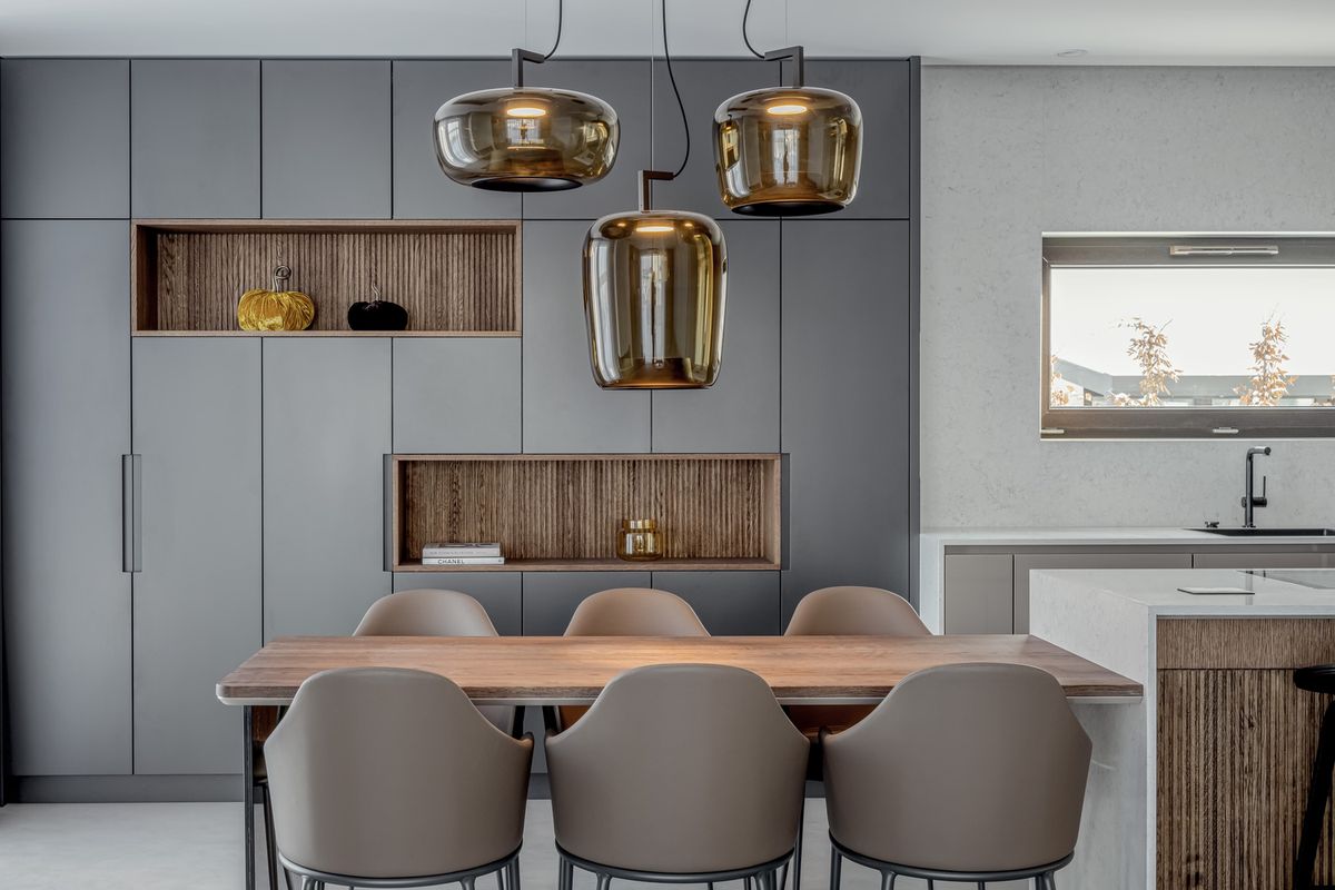 Luxurious kitchen with matt grey cabinetry, Brokis Double pendants, and a wooden table surrounded by taupe chairs.