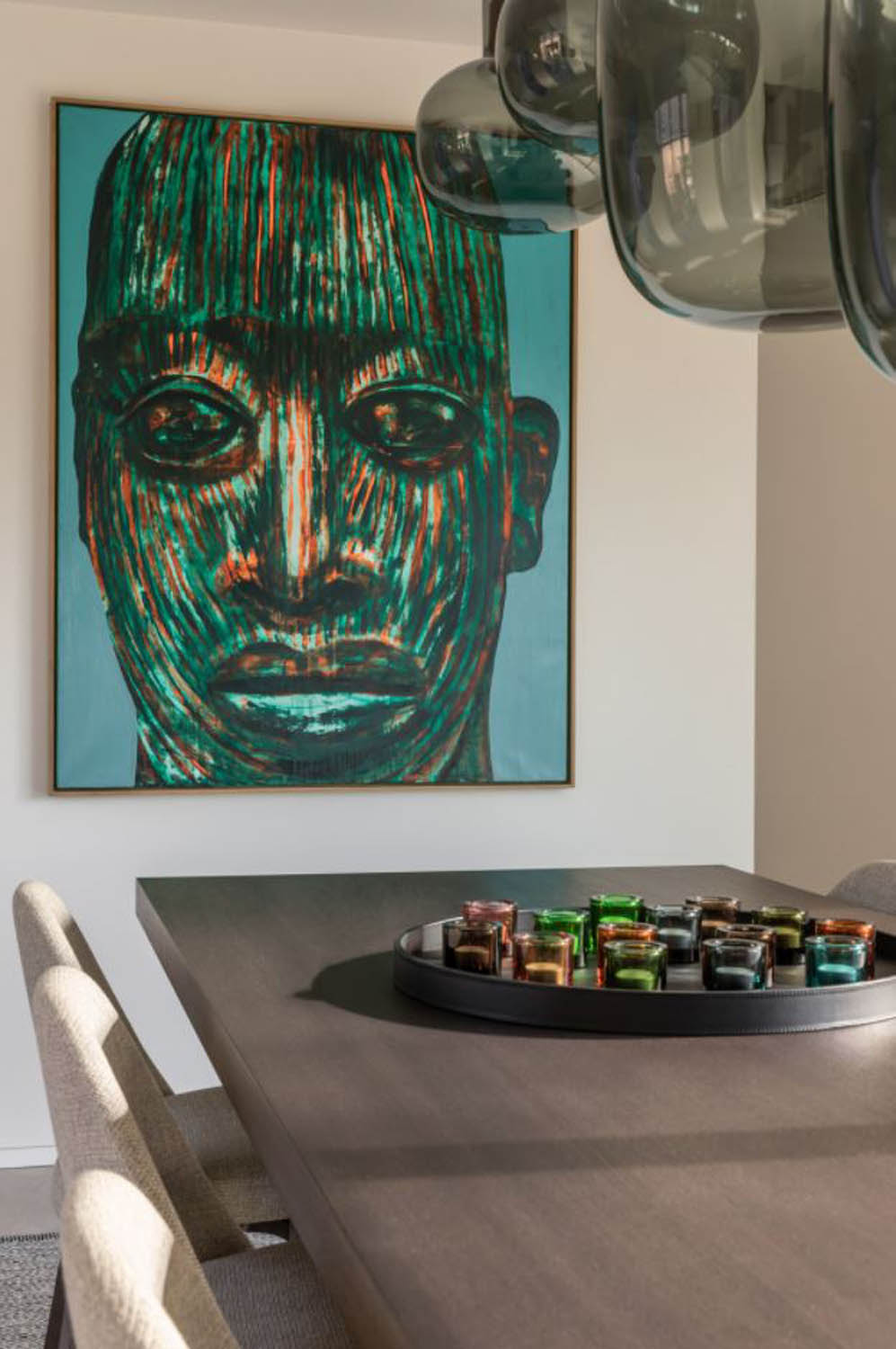 A modern dining room with a bold striped portrait, dark wood table, Brokis Awa pendants, and chic neutral chairs.