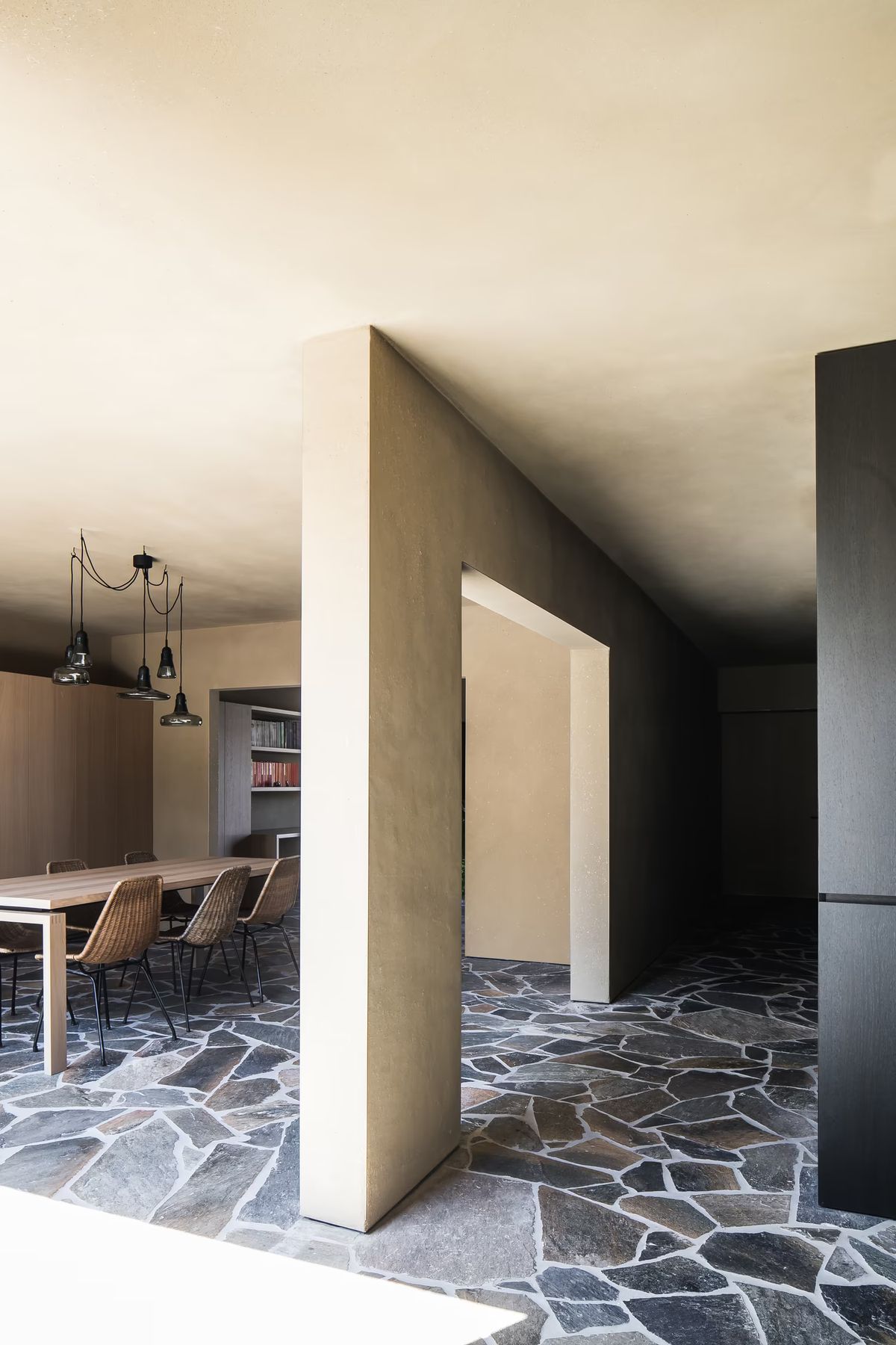 A modern space with beige walls, a dark stone floor, and Brokis Shadows Set Free above a wooden table.
