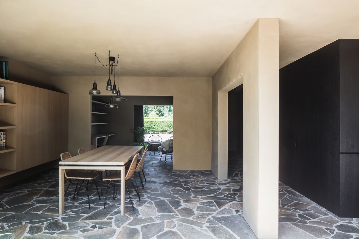 A modern dining room with stone tile floors, a light wood table, six chairs, Brokis Shadows Set Free, and elegant open views.