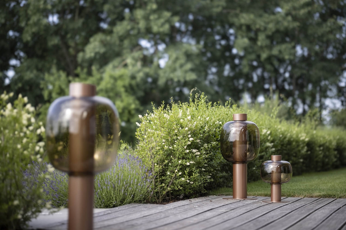 Brokis Bonbori Outdoor lanterns line a wooden deck amid lush lavender, manicured shrubs, and verdant garden greenery.