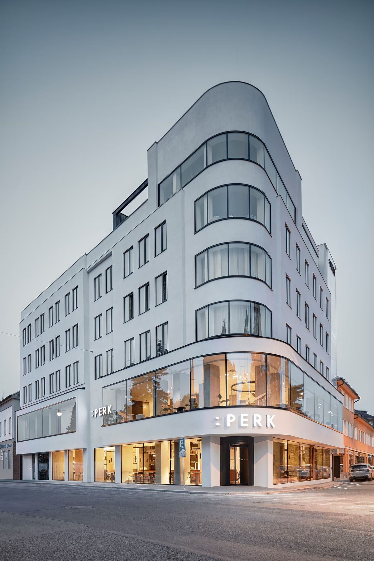 Hotel Perk modern multi-storey corner building with sweeping curved windows, glass shopfronts, on a chic city street.
