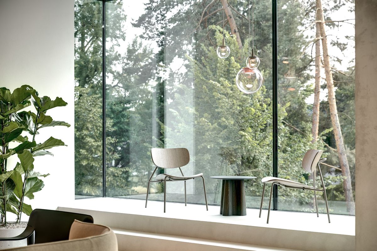 Minimalist seating area with two modern chairs, small round table, and Brokis Orbis pendants by a large window.