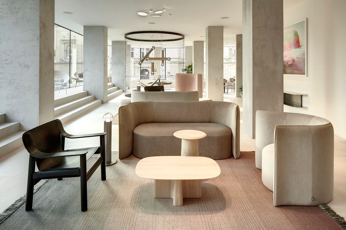A luxe, airy living room with curved neutral sofas, a black armchair, Brokis Prisma lights above pale wood tables.