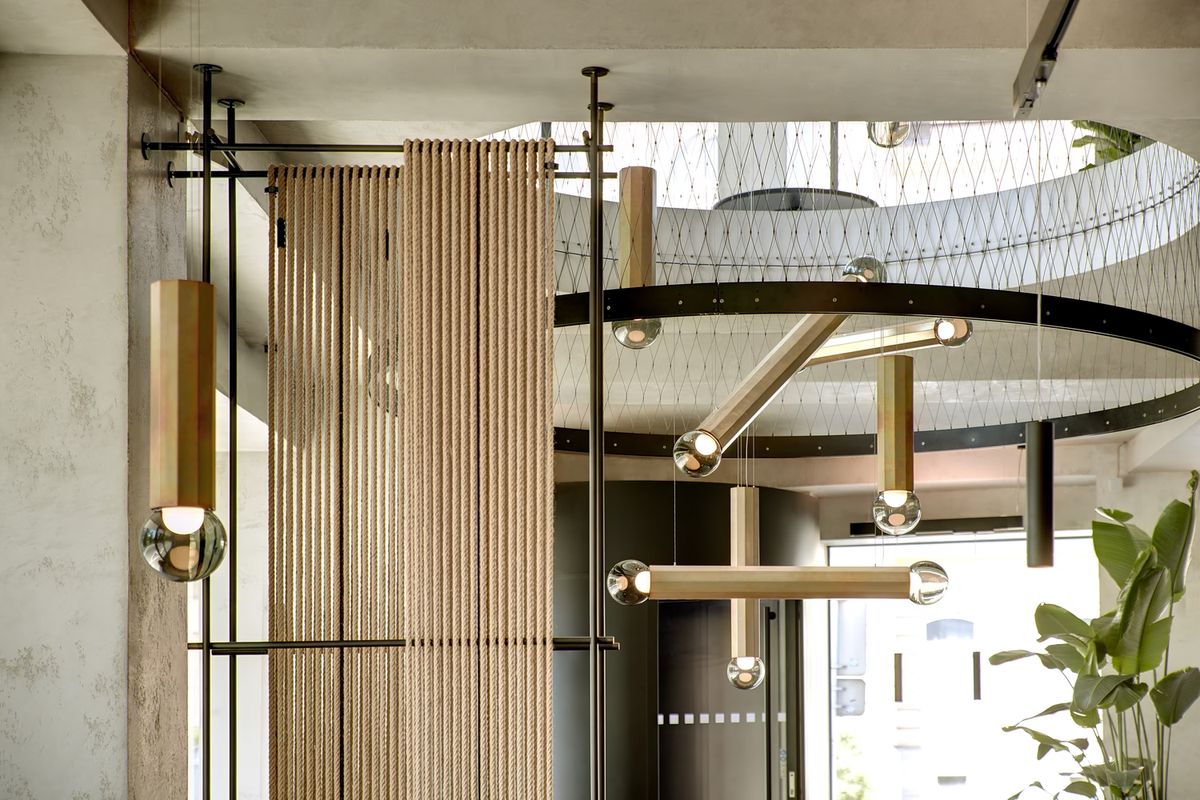 Elegant interior with Brokis Prisma lighting, clear globes, rope divider, lush leaves, and soft daylight.