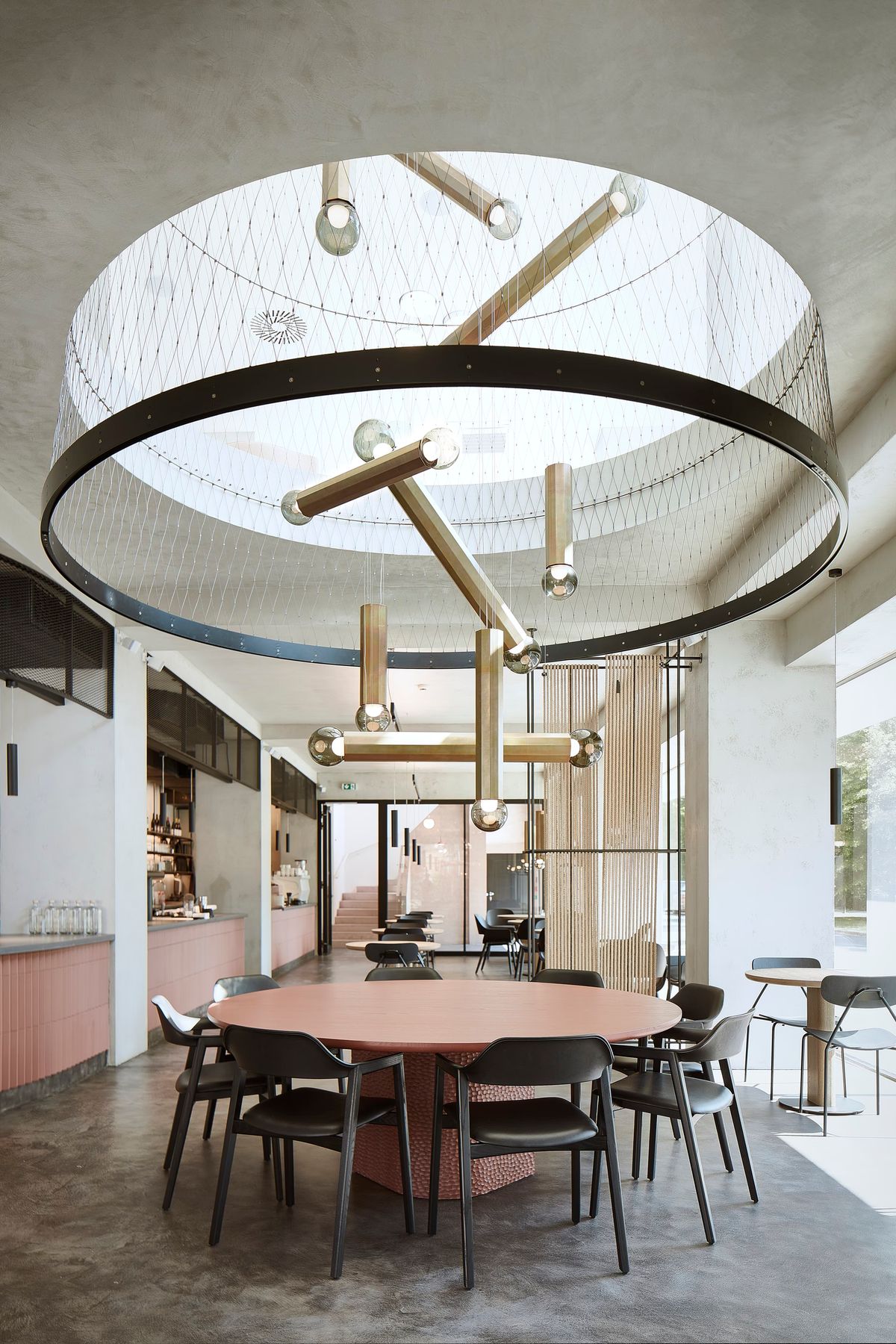 Luxurious dining space with a round table, black chairs, and Brokis Prisma lighting under a skylight.